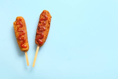 Mavi arka planda ketçaplı lezzetli mısırlı sosisliler.