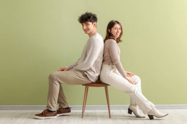 Yeşil arka planda bir sandalyede oturan şık elbiseli güzel bir çift.