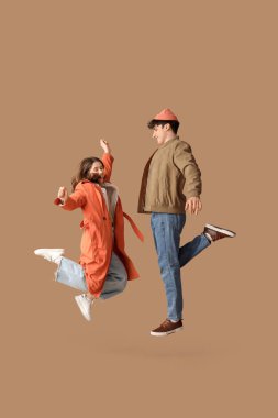 Bej arkaplanda zıplayan şık paltolu güzel bir çift.