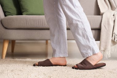 Evdeki kanepenin yanındaki yumuşak terlikli adam.