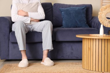 Yumuşak terlikli bir adam yastıklı koltukta oturuyor.