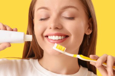 Sarı arka planda diş fırçası ve yapıştırmasıyla gülümseyen genç kadın, yakın plan.