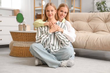 Güzel genç kız kardeşler oturma odasında sarılıyorlar.