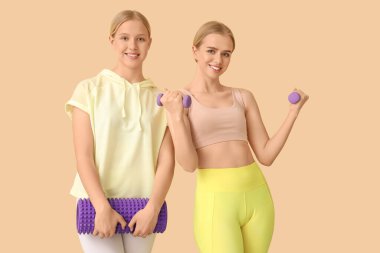 Bej arka planda egzersiz için aletleri olan güzel genç kız kardeşler.