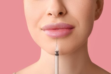 Güzel genç bir kadın pembe arka planda dudaklarından enjeksiyon yaptırıyor.