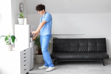 Erkek stajyer doktor klinikteki soğutucudan su dolduruyor.
