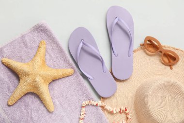 Beyaz arka planda deniz yıldızı, güneş gözlüğü, hasır şapka ve havlu olan parmak arası terlikler.