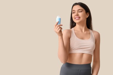 Young woman with deodorant on beige background