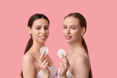 Sağlıklı cilt ve pembe arka planda pamuk pedleri olan güzel, genç ve mutlu kadınlar.