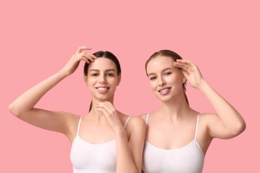 Pembe arka planda sağlıklı ciltli güzel, genç ve mutlu kadınlar.