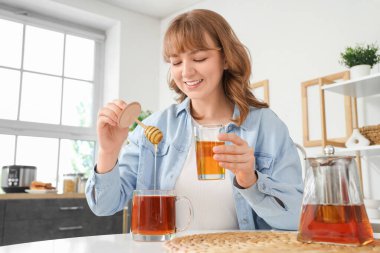 Genç bir kadın mutfaktaki çaya bal ekliyor.