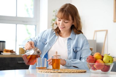 Genç bir kadın mutfaktaki çaydanlıktan fincana içecek dolduruyor.