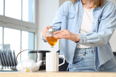 Genç bir kadın mutfaktaki çaya bal ekliyor.