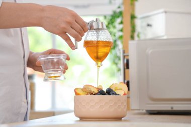 Genç kadın mutfaktaki lezzetli yulaf ezmesine tatlı bal ekliyor.