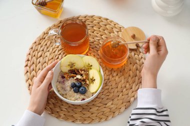 Bir kadın masadaki lezzetli yulaf ezmesine bal ekliyor.