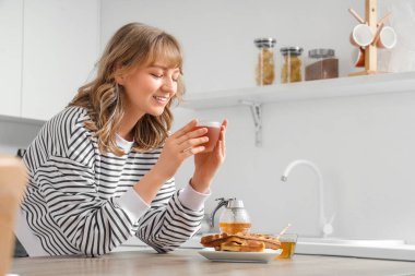 Bir fincan çayla genç bir kadın, mutfakta tatlı bal ve waffle.