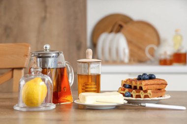 İçecekli çaydanlık, bal kavanozu, limon, tereyağı ve tatlı waffle mutfakta.