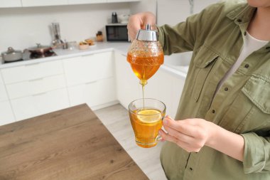 Genç bir kadın mutfaktaki çaya bal ekliyor.