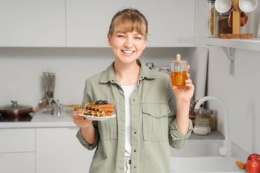 Mutfakta bir kavanoz lezzetli ballı ve tatlı waffle yapan genç bir kadın.