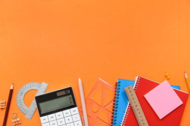 Turuncu arka planda hesap makinesi ve okul kırtasiyesi