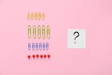 Pembe zemin üzerinde raptiyeler ve soru işareti olan kağıt parçaları.