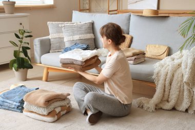Kadın evde otururken temiz giysileri katlıyor.