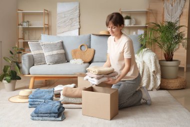 Kadın evde temiz kıyafetleri karton kutulara katlıyor.
