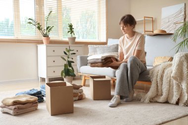 Kadın evde temiz kıyafetleri karton kutulara katlıyor.