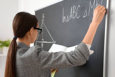 Sınıfta yazı tahtasının yanında genç bayan matematik öğretmeni.