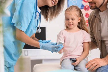 Kan şekerini ölçen kadın endokrinolog. Küçük kız ve babası klinikte.