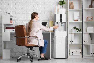 İş kadını ofisteki soğutucudan su dolduruyor.