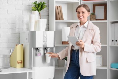 Tabletli iş kadını ofisteki soğutucudan su dolduruyor