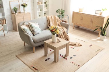 Yastıklı kanepe, ekose ve vazodaki yabani çiçekler oturma odasındaki sehpanın üzerinde.