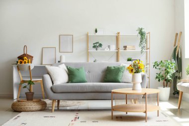 Oturma odasının iç tarafındaki sehpada yabani çiçekler olan rahat bir kanepe ve vazo.