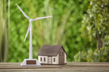 Rüzgar türbini ve ev modelleri yeşil doğaya karşı ahşap masada.