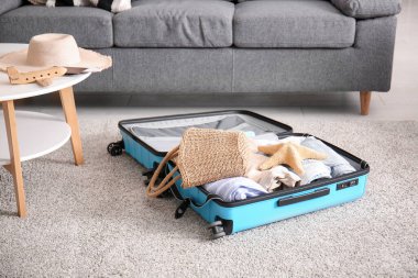 Oturma odasının zemininde giysi ve plaj aksesuarlarıyla dolu bir bavul. Yaz tatili kavramı