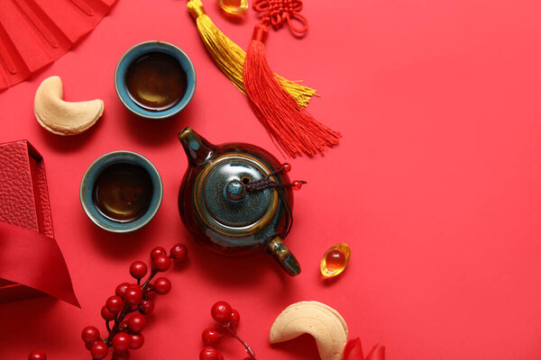 Чайник с чашками чая, печенье судьбы и различные китайские символы на красном фоне. Новогодний праздник