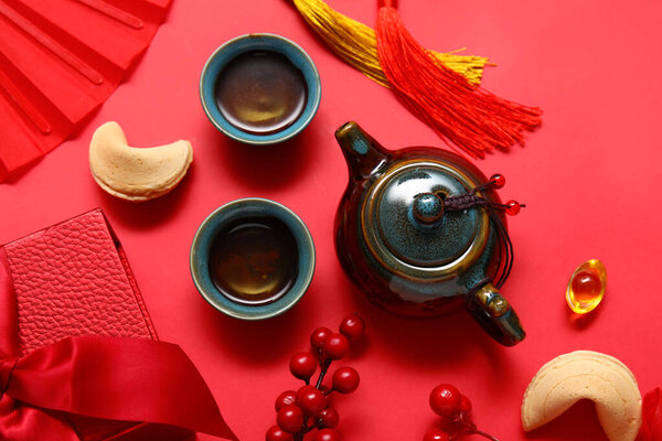 Чайник с чашками чая, печенье судьбы и различные китайские символы на красном фоне. Новогодний праздник