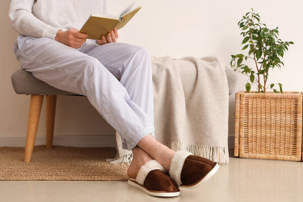 Человек с книгой в тапочках сидит на мягкой скамейке в комнате