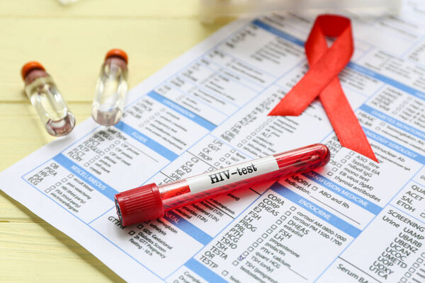 HIV blood test tube, laboratory report form and red ribbon on yellow wooden background