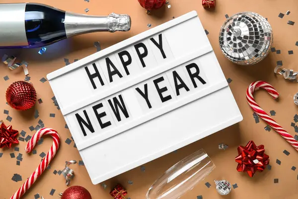 Mutlu yıllar yazılı pano, Noel baloları, baston şekerler ve bej arka planda bir şişe şampanya.