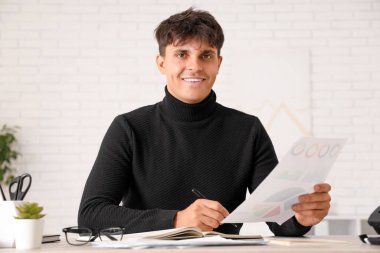 Ofisteki masalarda diyagramlarla çalışan yakışıklı bir iş adamı.