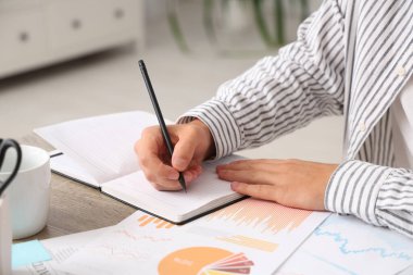 Ofisteki masada deftere yazan erkek ekonomist, yakın plan.