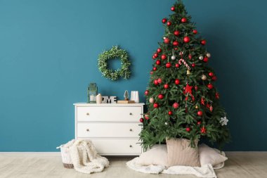 Şifoniyerli Noel ağacı ve mavi duvarın yanındaki süslemeler.