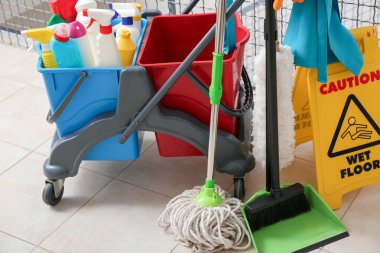 Temizlik malzemeleri, yer paspası ve ofisteki merdivenlere uyarı levhası konmuş kapıcı vagonu.