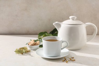 Bir fincan lezzetli ıhlamur çayı, çaydanlık ve beyaz arka planda yapraklar.