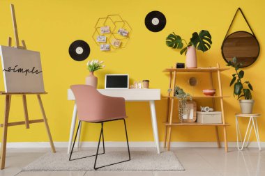 Modern dizüstü bilgisayarı, vinil diskleri ve sarı duvarda asılı ruh hâli tahtası olan şık çalışma alanının içi.