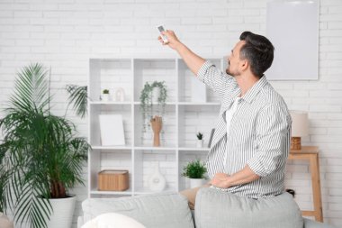 Yakışıklı genç adam oturma odasındaki beyaz duvarın yanında klimayı açıyor.