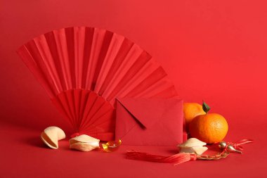 Kırmızı arka planda Çin sembolleri, mandalinalar ve fal kurabiyeleri olan kırmızı bir zarf. Yeni yıl kutlaması