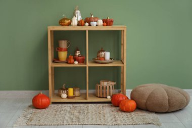 Balkabağı, dekor şeklinde mumları olan raf ünitesi ve yeşil duvarın yanında puf.